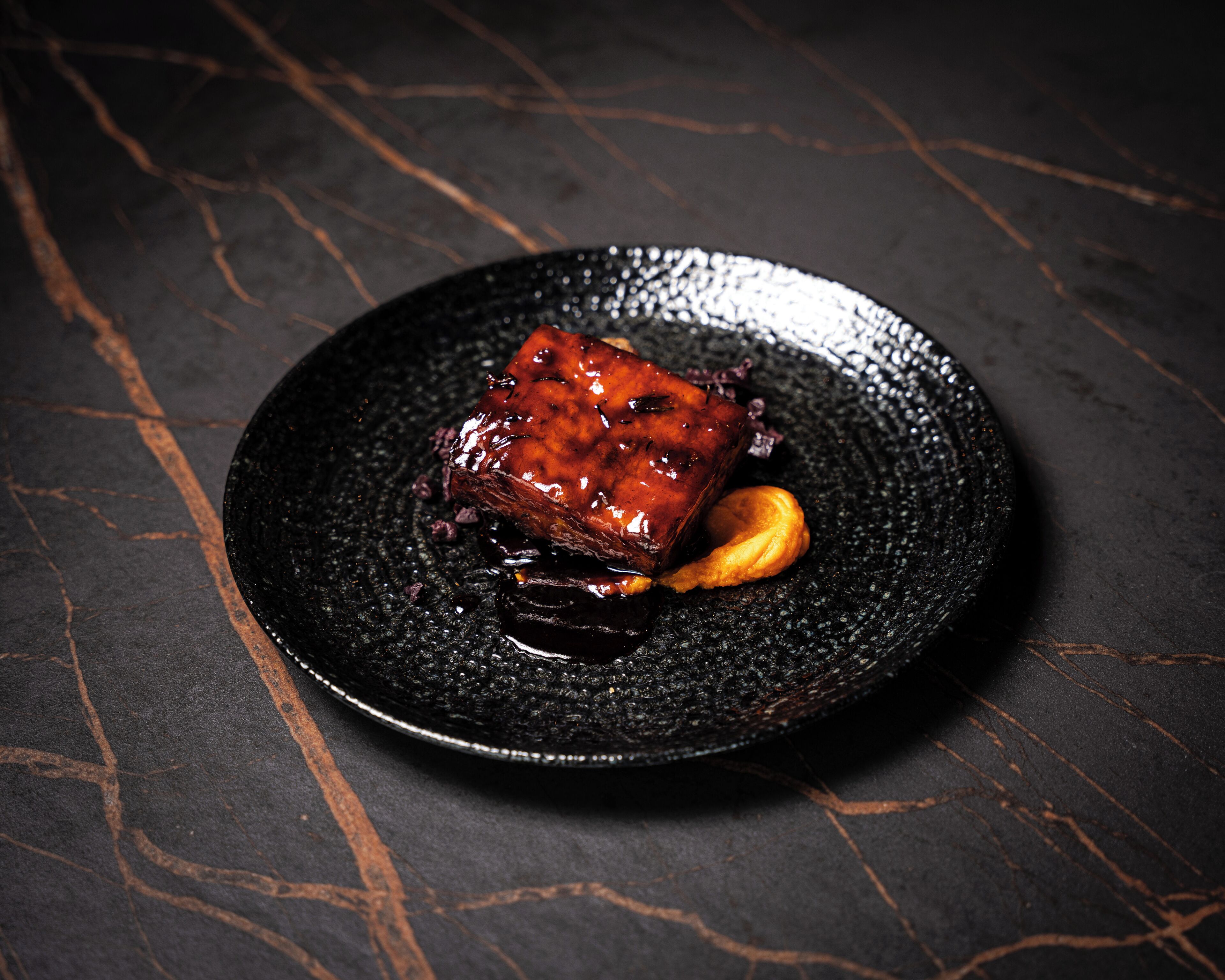 Un dessert servi dans une assiette noire à texture, sur un fond sombre.