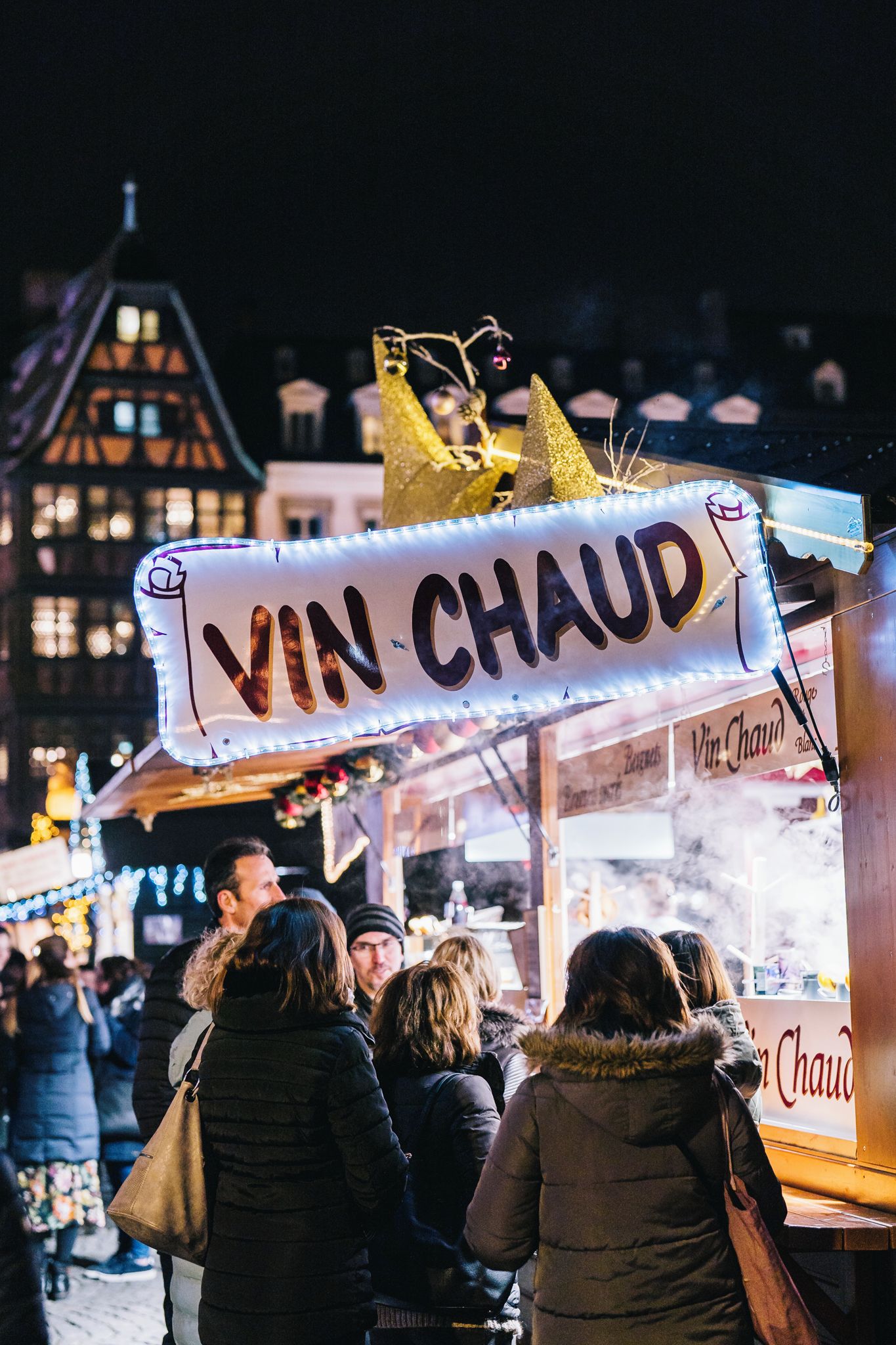 A street food stall with a sign reading 'VIN-CHAUD' and a crowd of people.