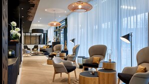 Un salón moderno con muebles contemporáneos, ventanas amplias con cortinas traslúcidas e iluminación colgante elegante.