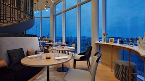 Un restaurante moderno con mesas redondas, asientos cómodos y grandes ventanales con vistas a la ciudad.