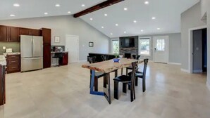 A spacious kitchen with a dining area, wooden ceiling beams, and recessed lighting.