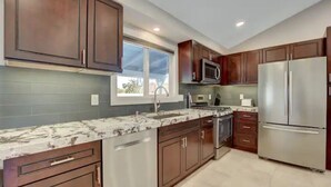 A modern kitchen with stainless steel appliances, wooden cabinets, and a large window providing natural light.