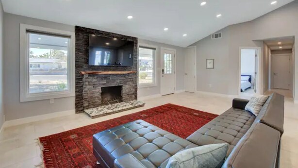 A spacious living room with a stone fireplace, a large grey sofa, and a red rug.