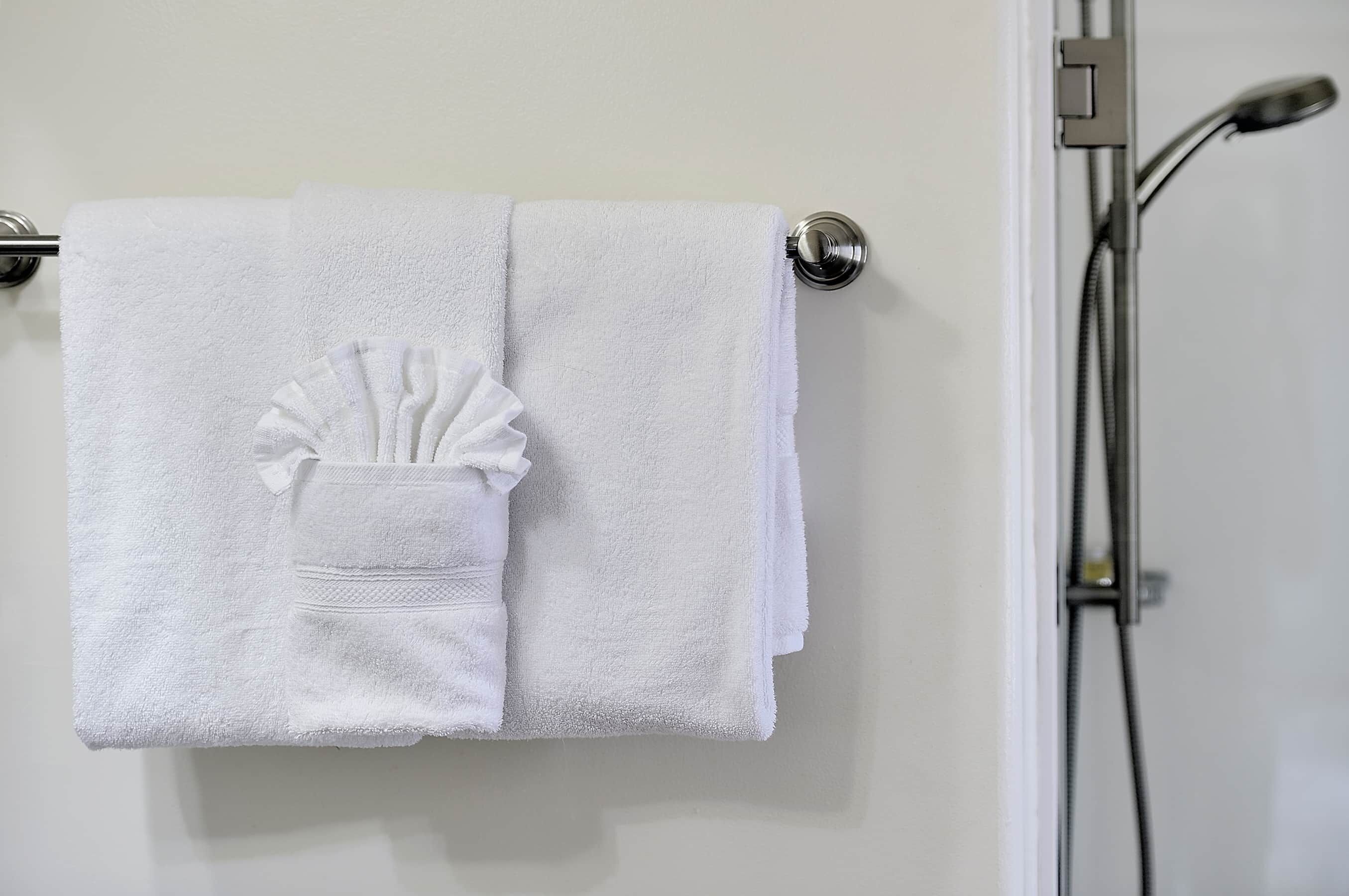 A white towel with a decorative bow on a metal towel bar in a bathroom.