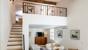 A spacious living area with a staircase leading to a loft bedroom, a wooden dining table, and a television in the background.