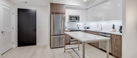 A modern kitchen with stainless steel appliances, a white countertop, and wooden cabinets.
