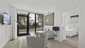 Habitación de hotel moderna con sofá, cama, televisor y un ventanal con vistas a árboles y edificios.