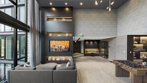 Un espacio lounge moderno con un sofá, una mesa de fútbol y una pantalla de televisión mostrando una caricatura.