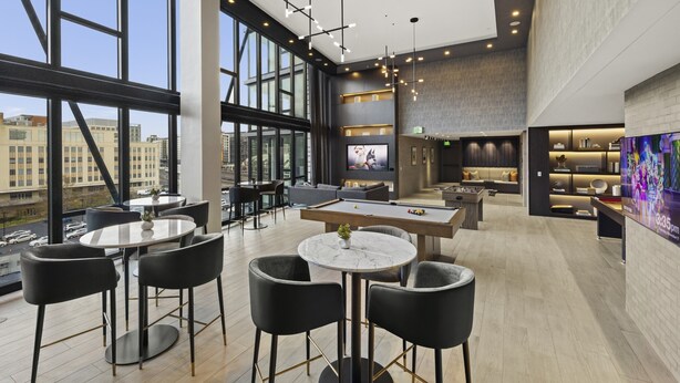 Un área lounge moderna con mesa de billar, asientos de bar y un amplio ventanal con vistas a la ciudad.