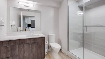 Et moderne badeværelse med en hvid vask, træskab, toilet og en bruseniche med glasvægge.