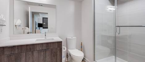 Une salle de bain moderne avec un lavabo blanc, un meuble-lavabo en bois, des toilettes et une douche séparée par une paroi de verre.