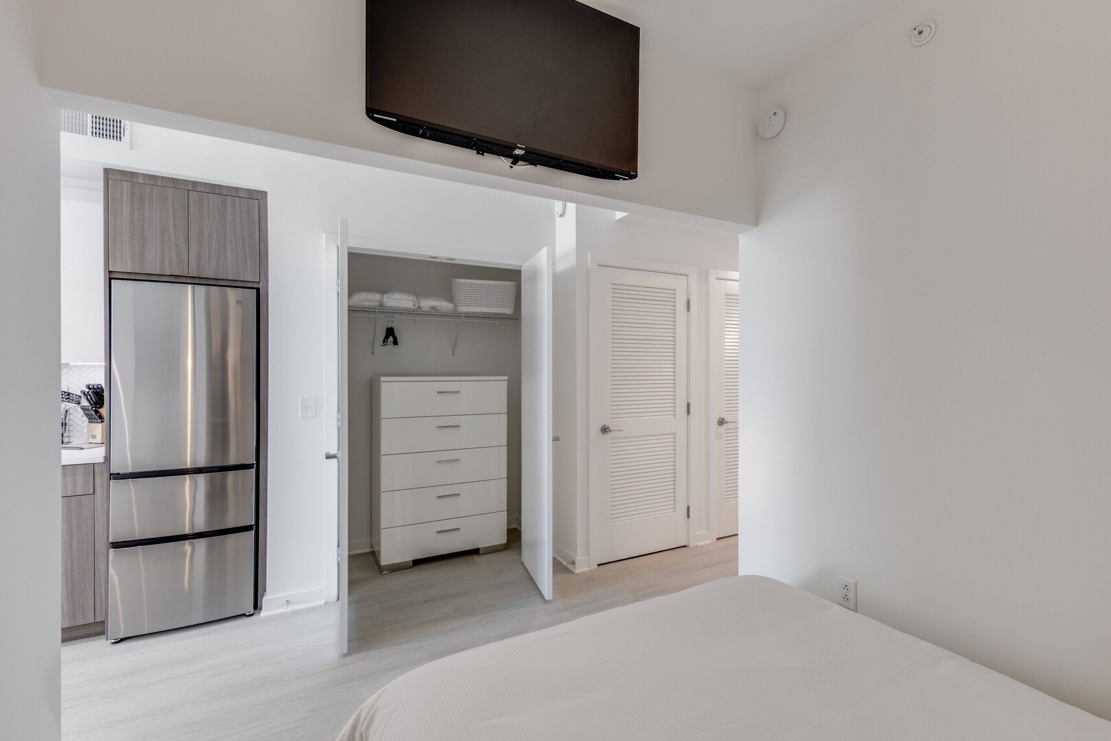 Una habitación de hotel moderna con kitchenette, televisor de pantalla plana, armario y cama.