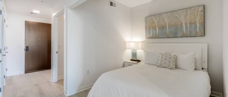 Un dormitorio con una cama grande, una mesita de noche con una lámpara, una puerta de madera y un cuadro en la pared.