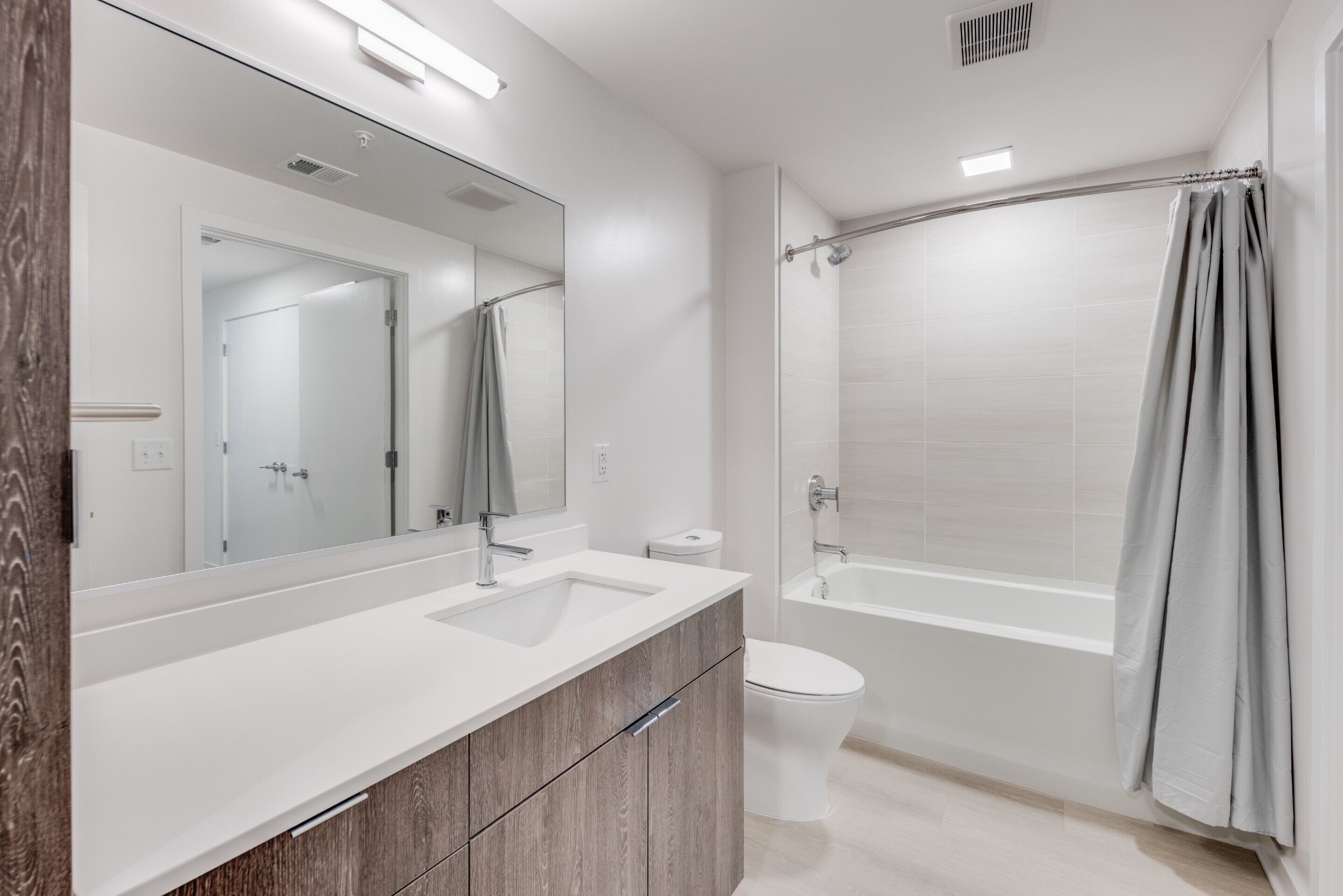 Een moderne badkamer met een grote spiegel, een wastafel, toilet en douche.