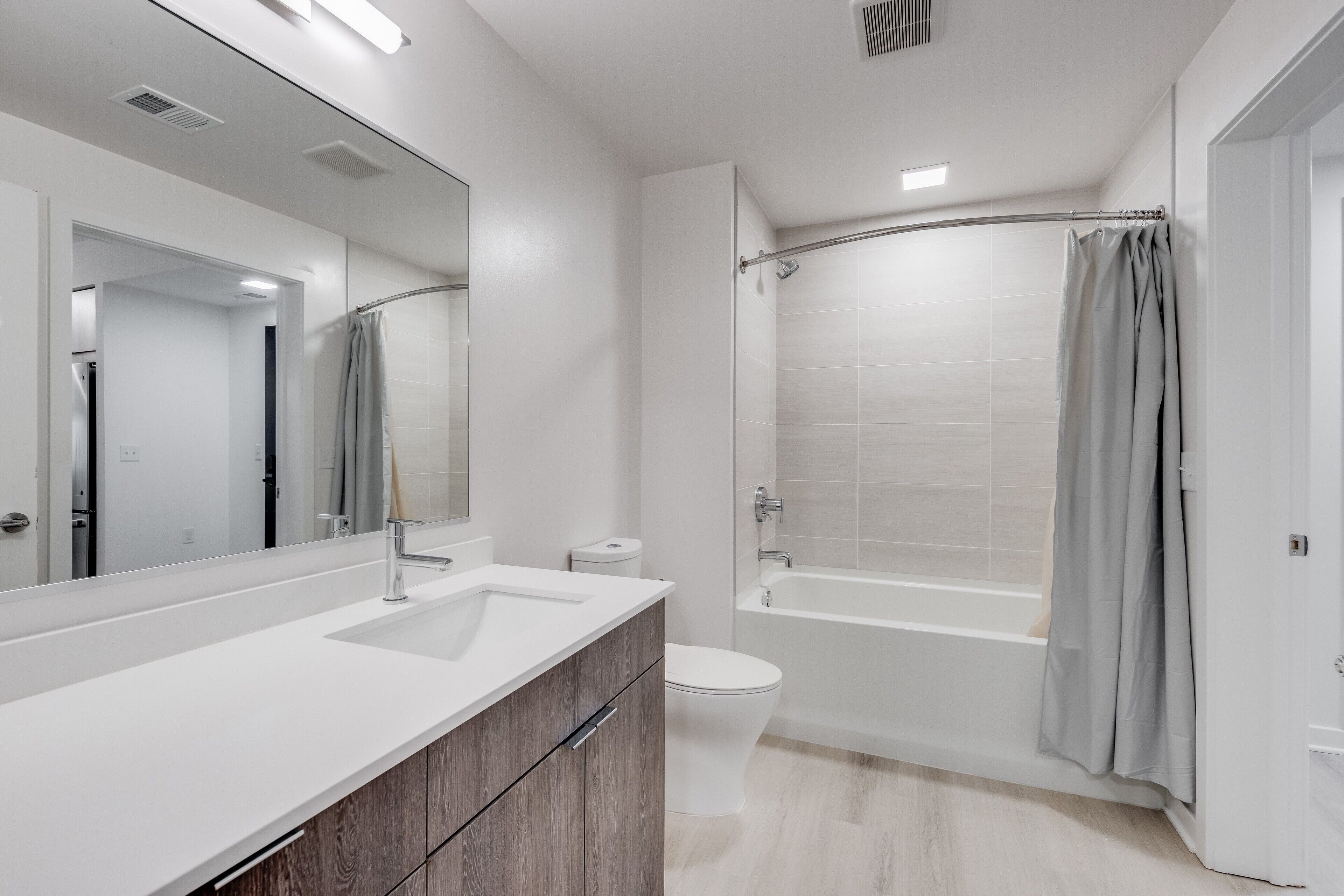 Un baño moderno con lavamanos, tocador, inodoro y ducha a ras de suelo con cortina.