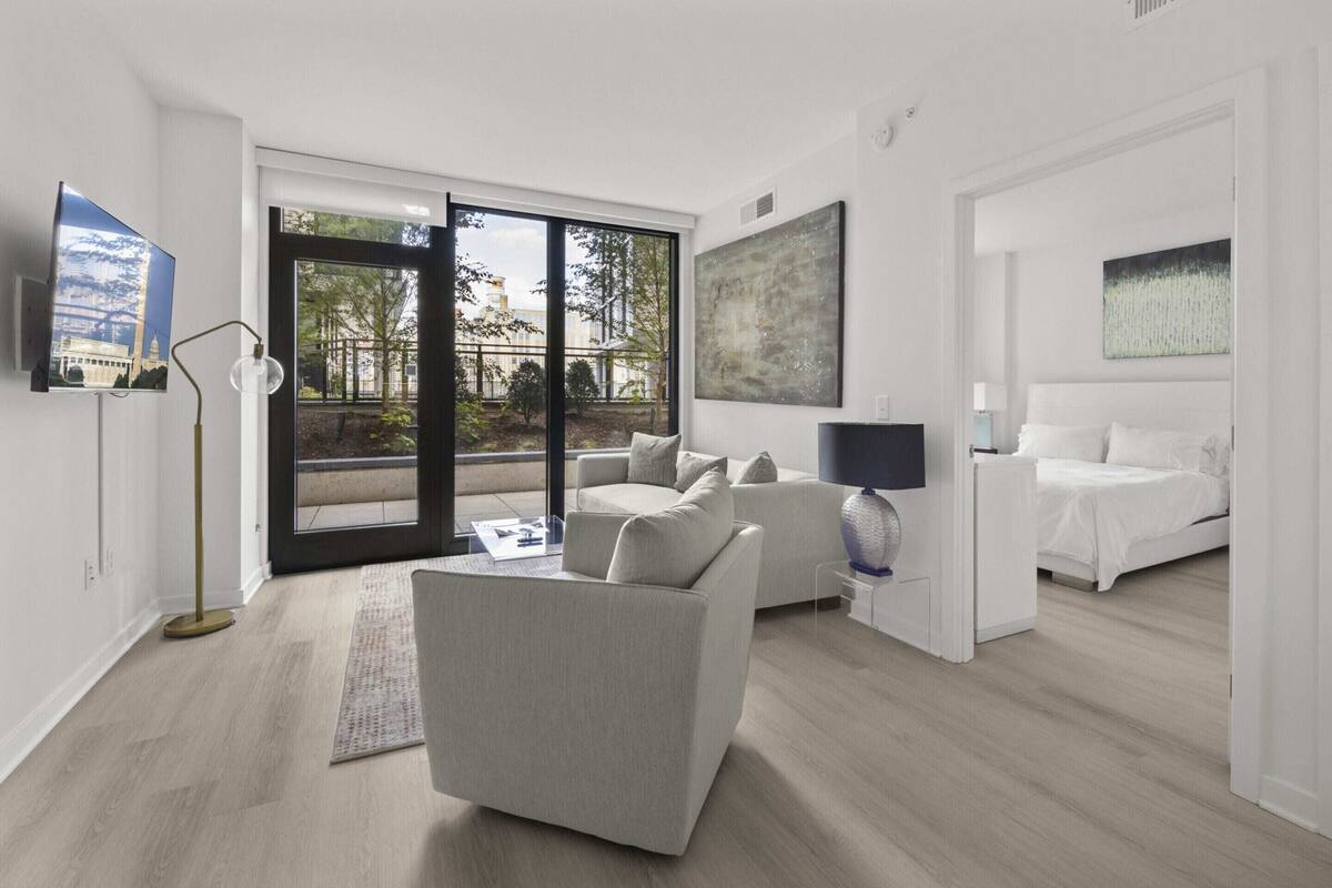 Habitación de hotel moderna con sofá, cama, televisión y un amplio ventanal con vistas a un edificio.