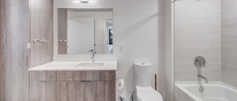 Een moderne badkamer met een houten wastafel, een witte wasbak, een toilet en een bad.