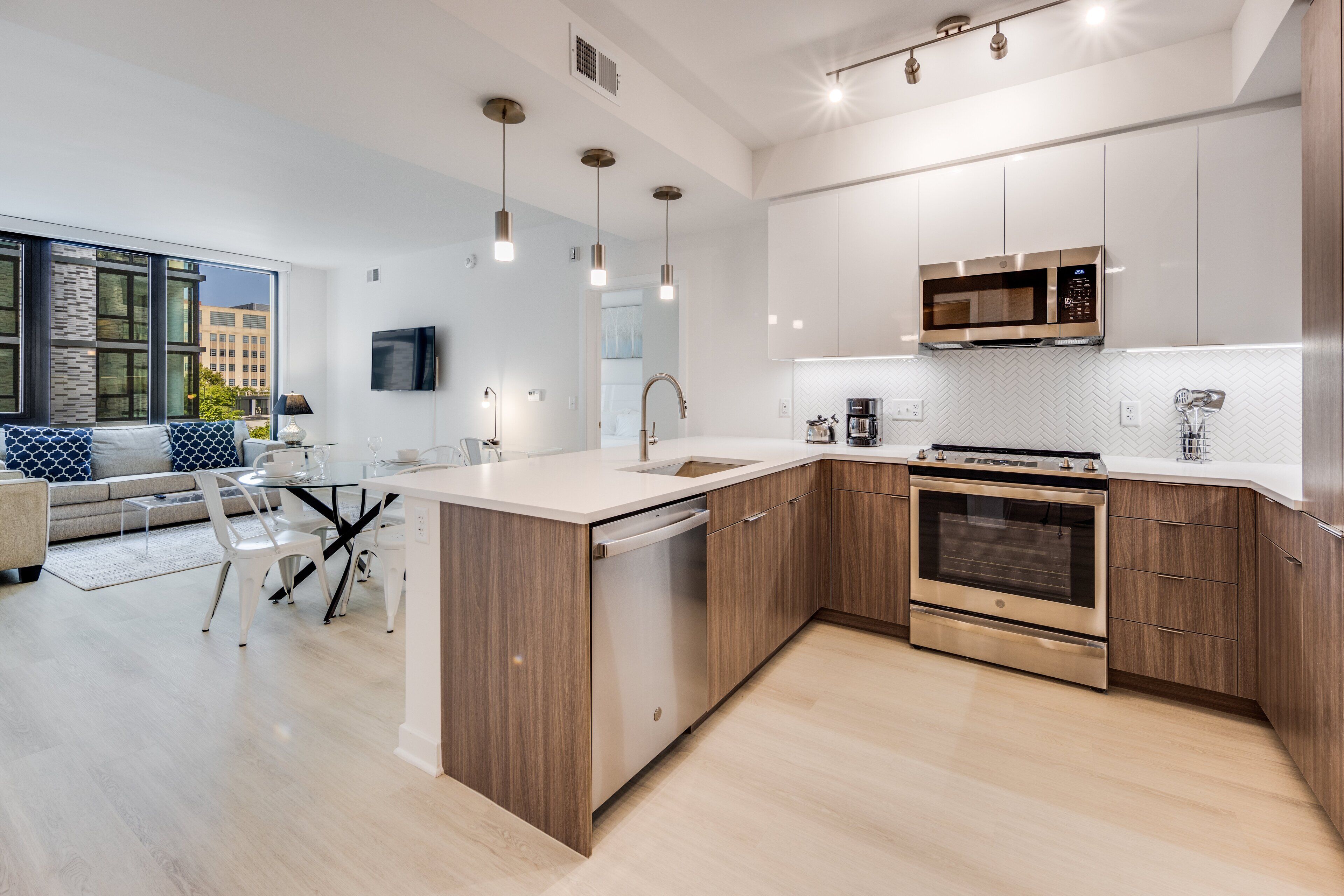 A modern kitchen with a dishwasher, oven, and microwave. There is a dining area with a table and chairs.