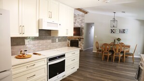 Une cuisine moderne avec des meubles blancs, un four encastré et un coin repas comprenant des chaises et une table en bois.