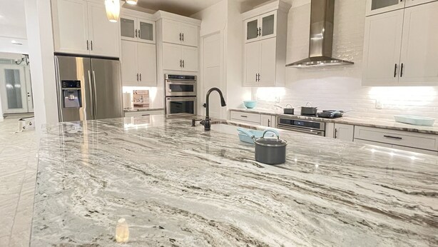A modern kitchen with white cabinets, a stainless steel refrigerator, an oven, and a large island with a marble countertop.