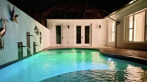 An indoor swimming pool with a tiled edge, a wooden deck area, and a door leading to another room.