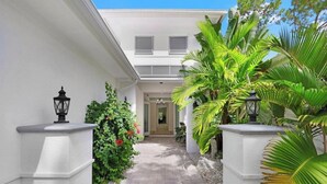 A pathway leading to a building with a white exterior, surrounded by lush greenery and two black lanterns on either side.