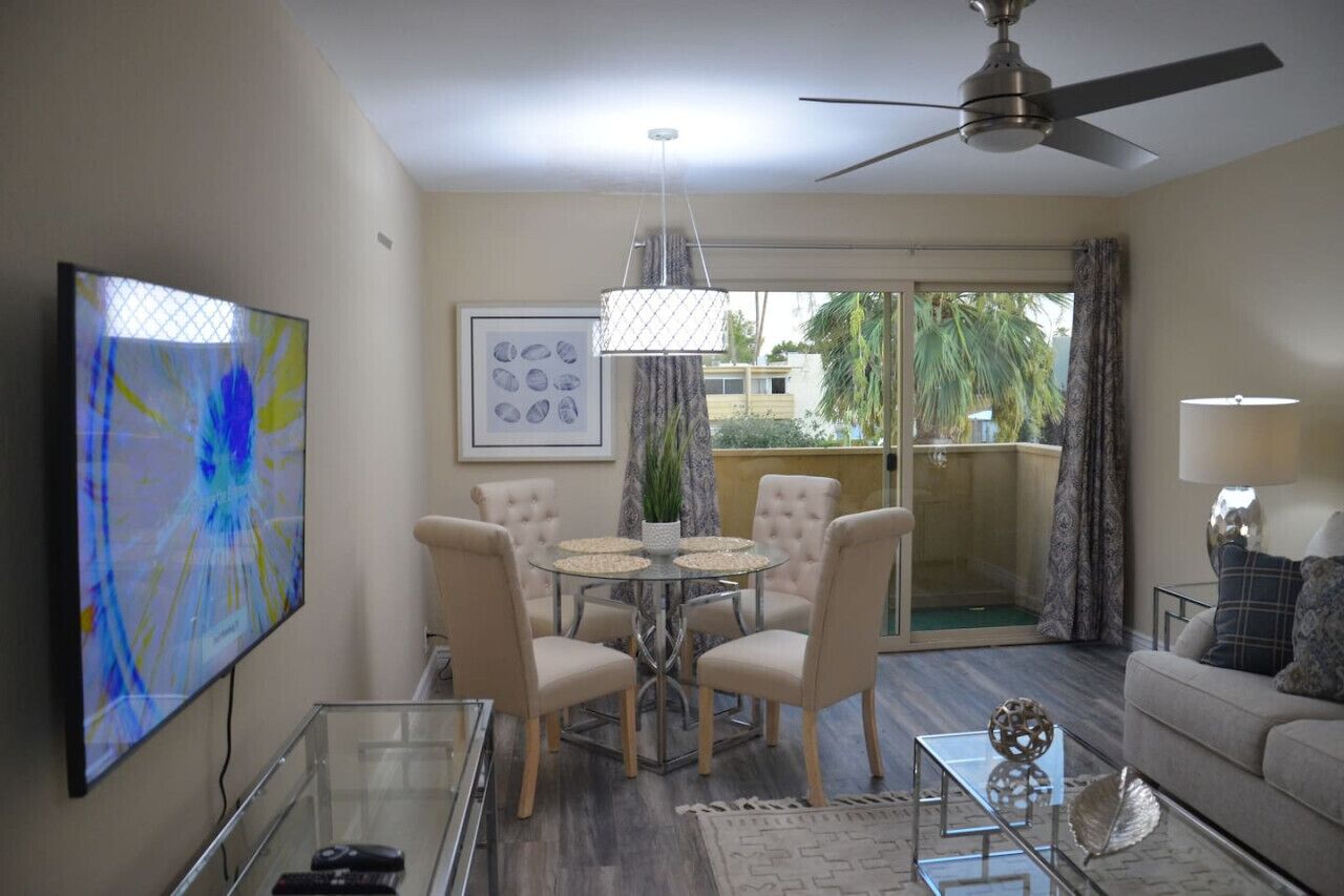Un salon avec un téléviseur, une table à manger avec des chaises, un ventilateur de plafond et un canapé.