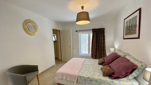 Un dormitorio con cama, una silla, una lámpara, una ventana con cortinas y una puerta.