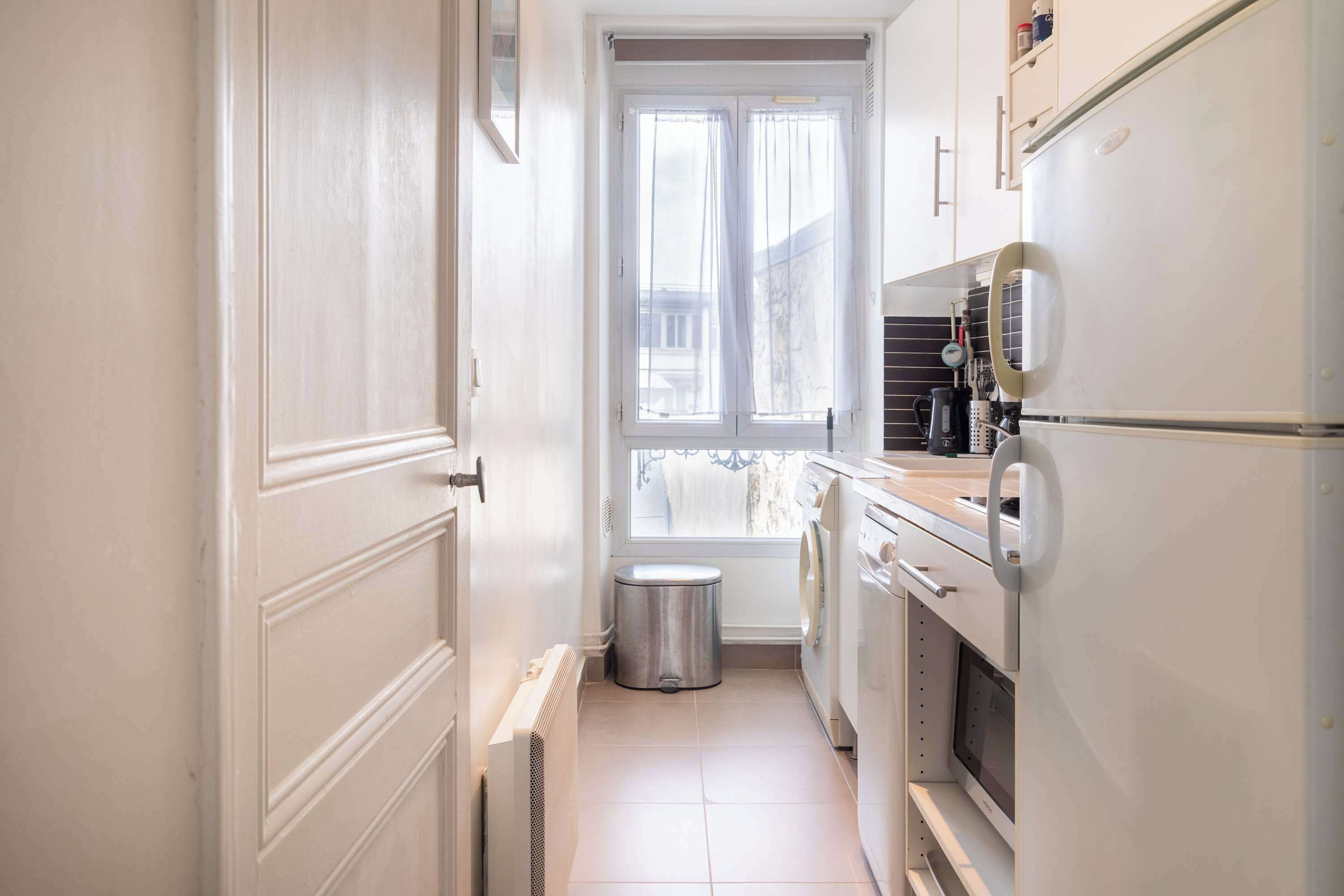 A narrow kitchen with a window, a washing machine, and a refrigerator.
