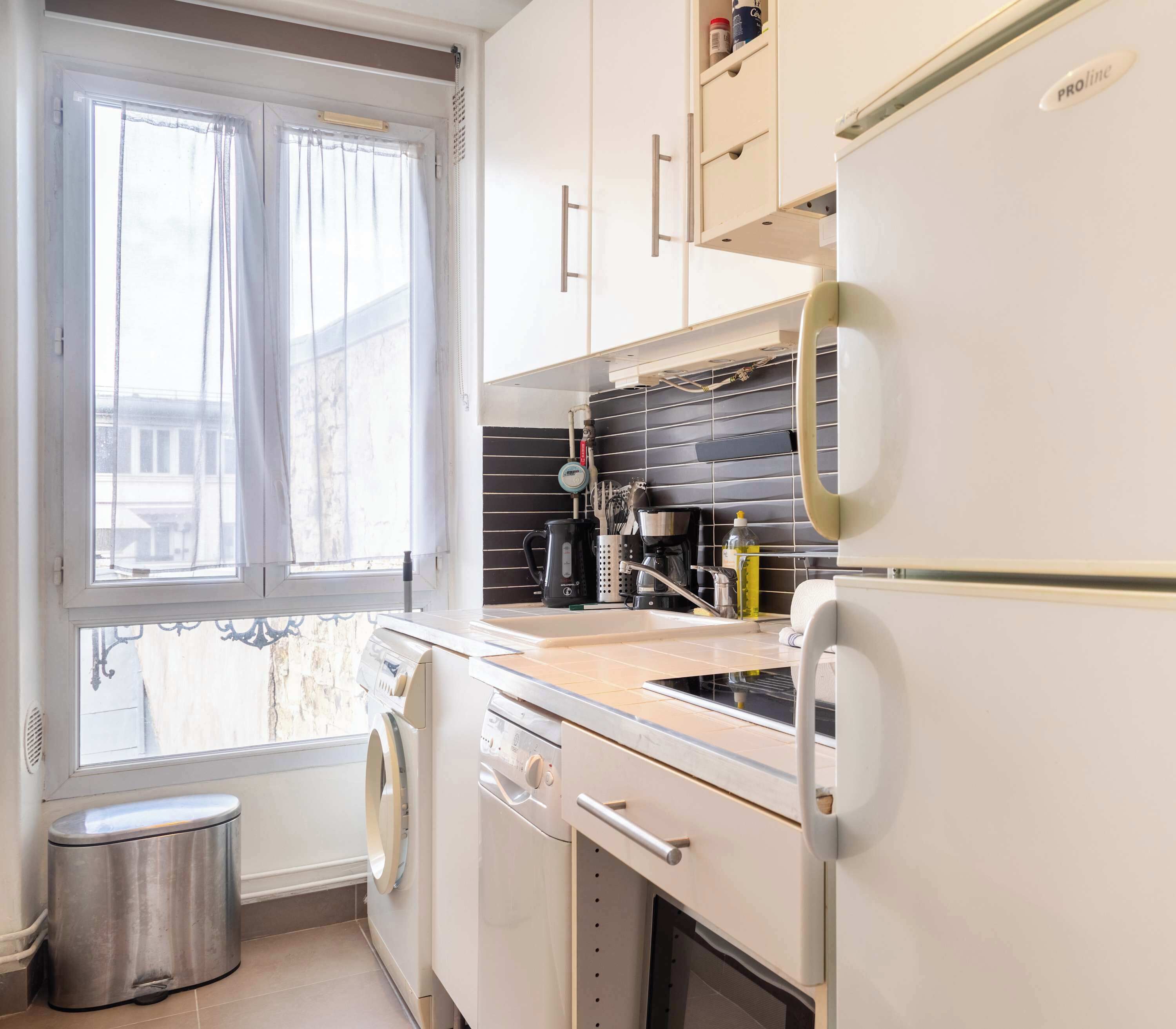 A compact kitchen with a window, a washing machine, a refrigerator, and a sink.