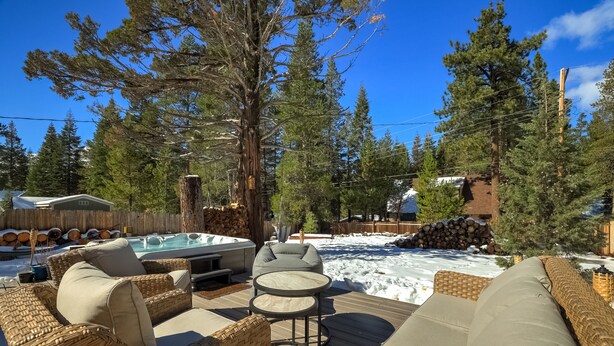 Eine Terrasse mit Korbmöbeln, einem Whirlpool und verschneiter Landschaft.