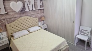 A bedroom with a tufted headboard, a bed with a patterned bedspread, a nightstand with a lamp, and a wardrobe. - Nina's house 2 300 meters from the sea (Santa Caterina Dello Ionio Marina)