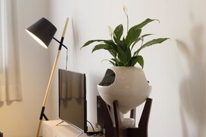 Een bloempot op een standaard, een vloerlamp en een televisie op een houten tafel.
