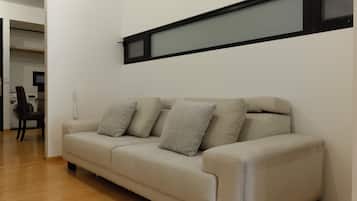 A beige sofa with three pillows, a wooden floor, and a wall-mounted shelf above.