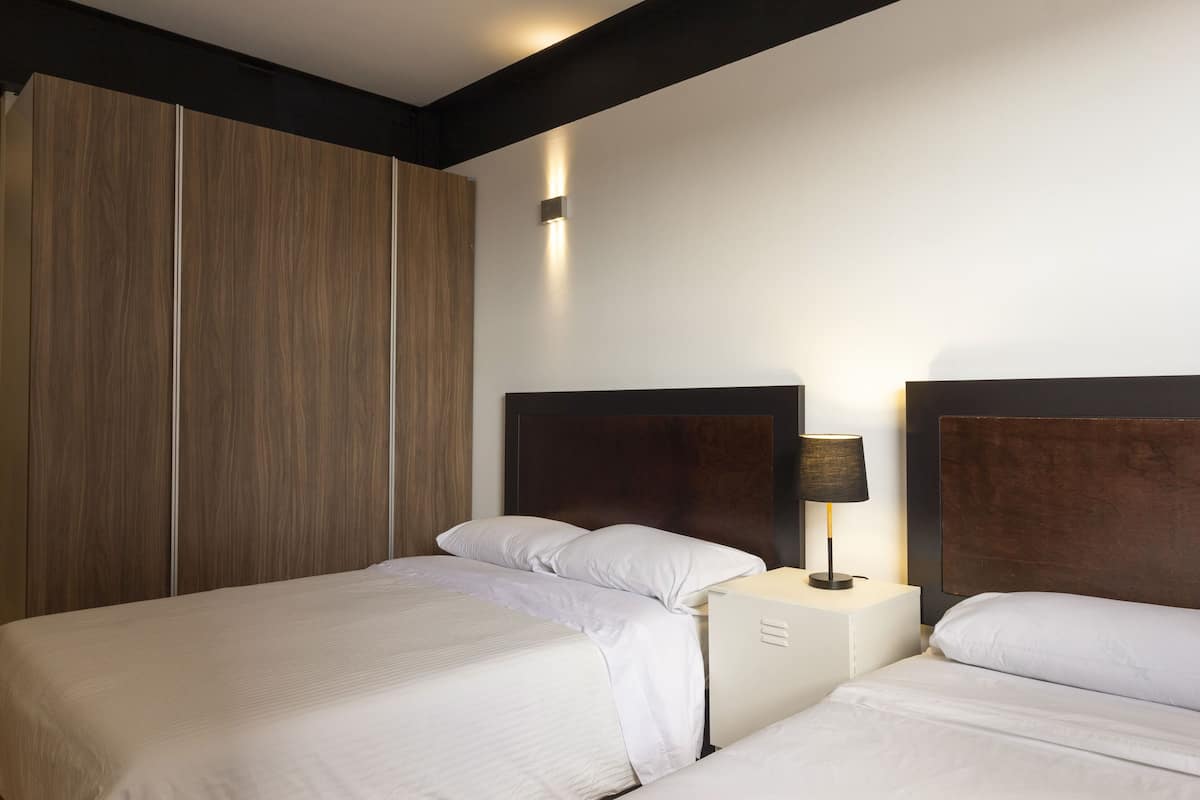 Quarto de hotel com duas camas, um guarda-roupa e uma mesa de cabeceira com abajur.