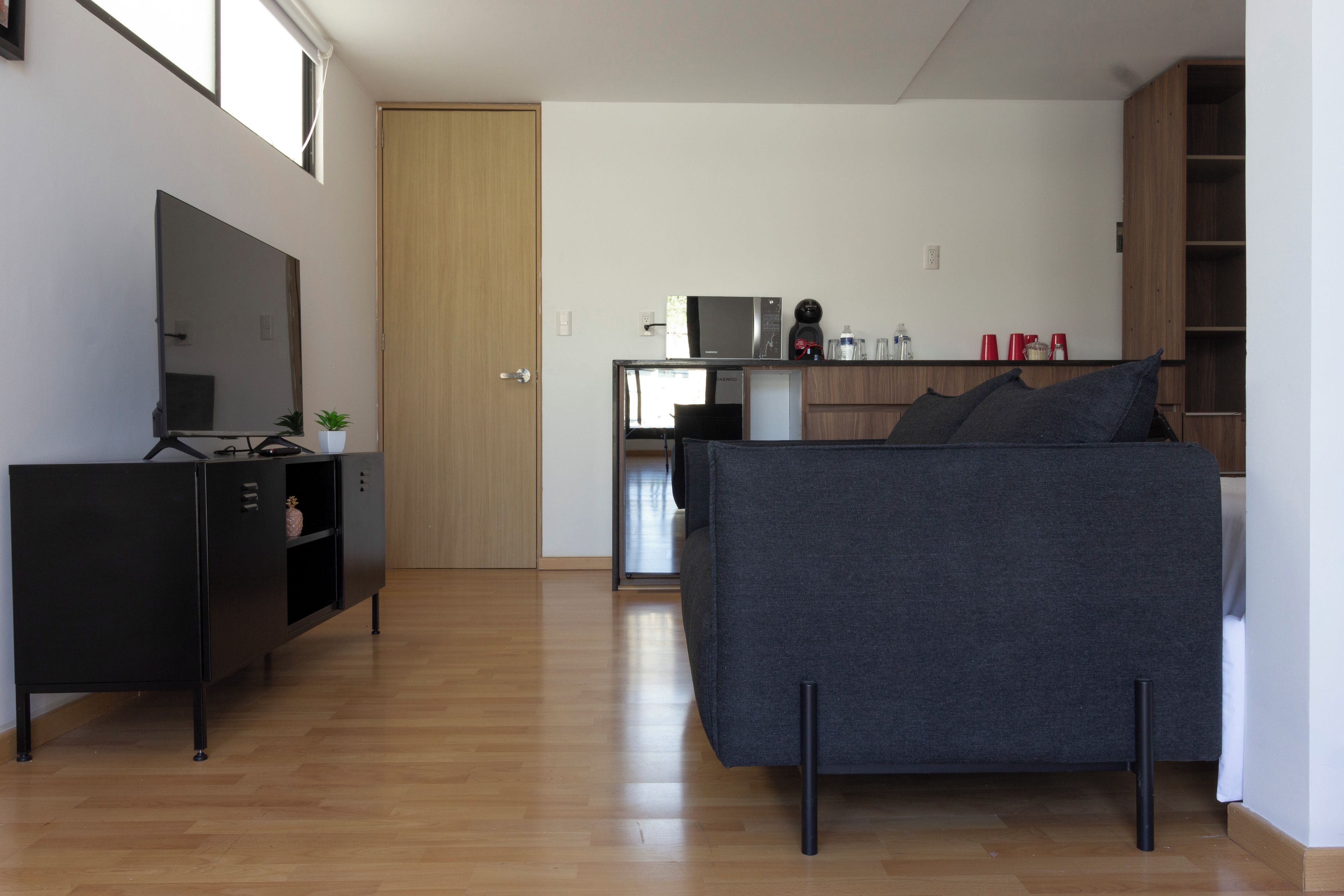 Un espacio habitable moderno con sofá, televisor, zona de cocina y puerta de madera.