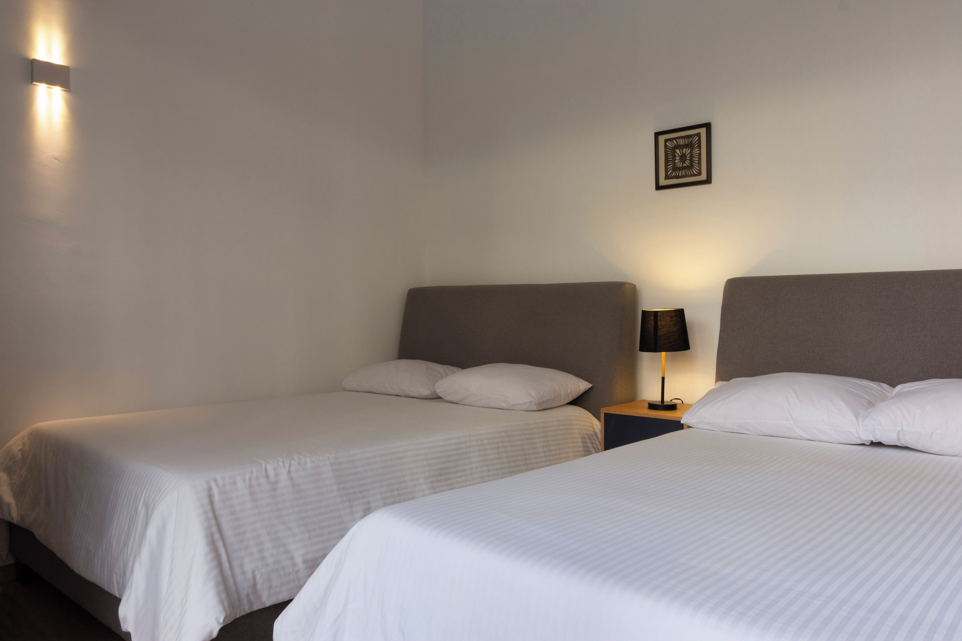 Una camera d'albergo con due letti singoli, un comodino con una lampada e un quadro appeso al muro.