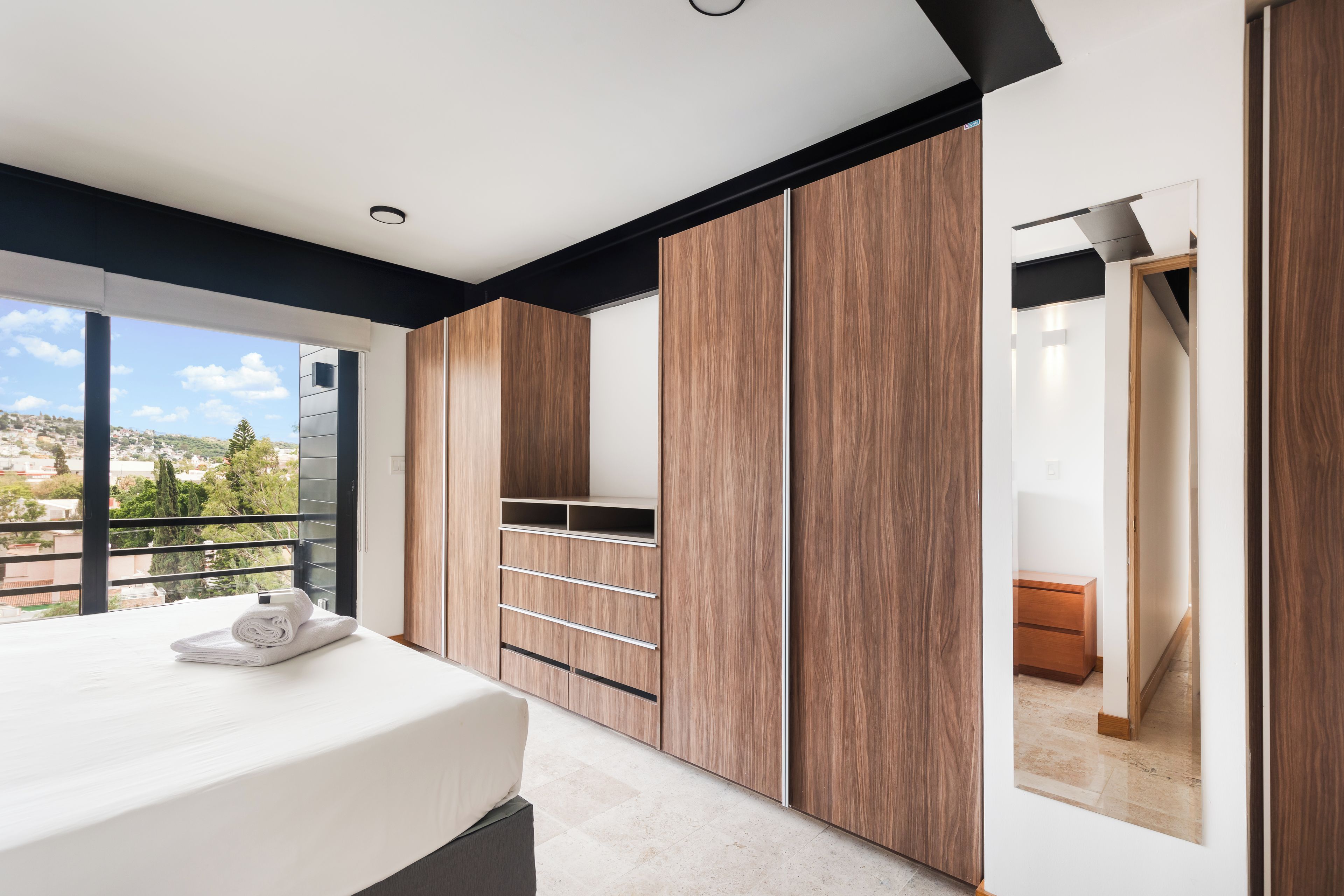 Un dormitorio moderno con una cama grande, armario empotrado y balcón con vista a la ciudad.