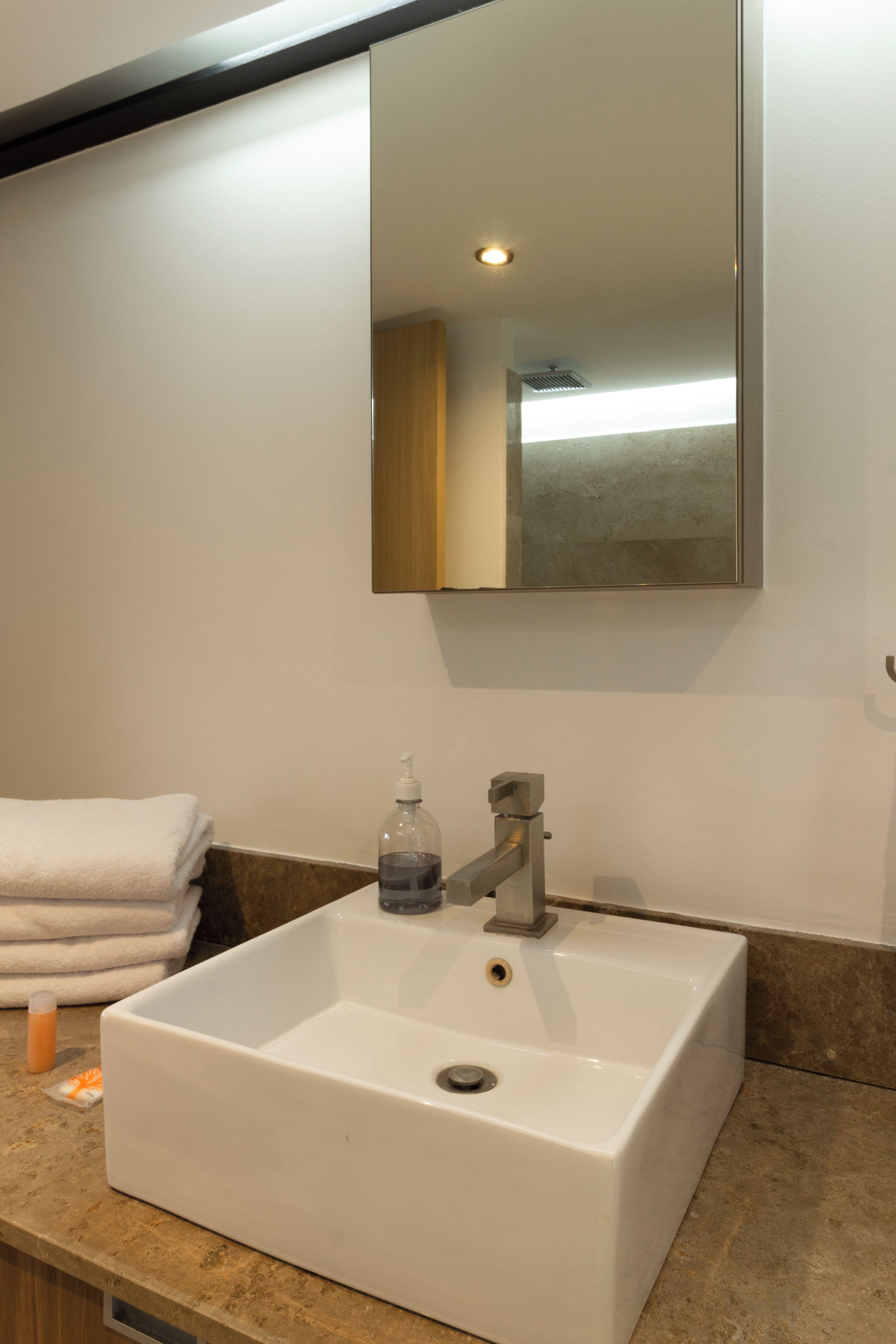 A bathroom with a white sink, a mirror, and a towel stack.