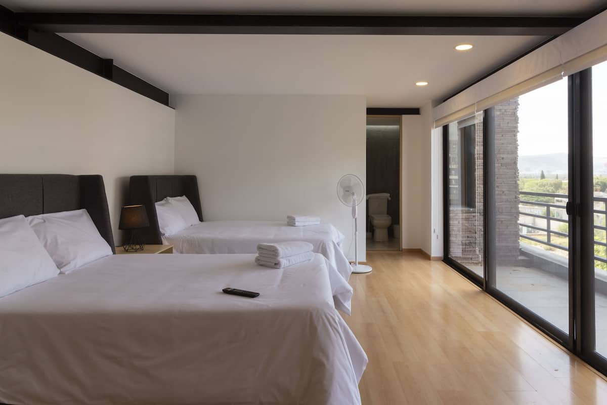 Quarto de hotel com duas camas, um ventilador e varanda com vista.