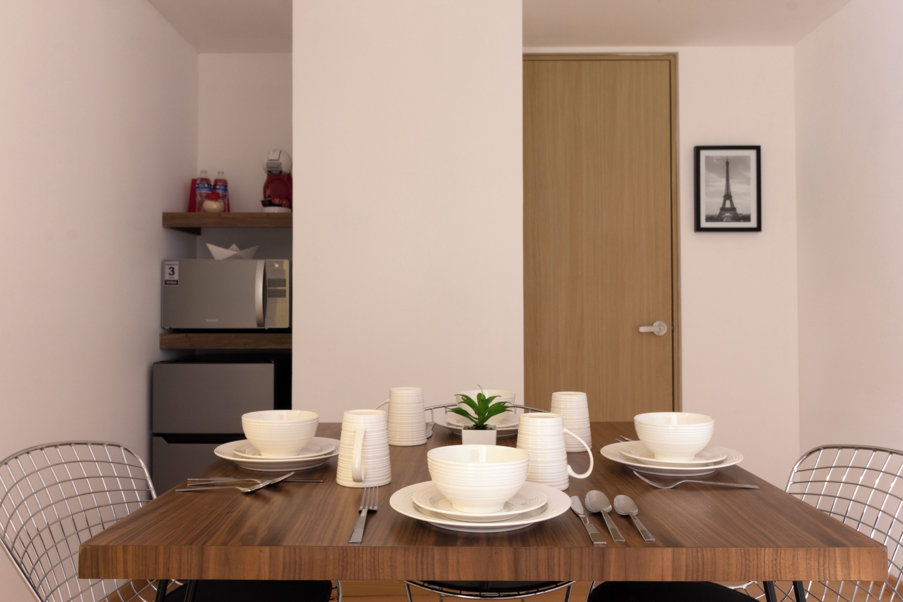 Une table à manger dressée avec de l’assiette, des bols et des couverts blancs, et une petite plante en pot posée sur la table.