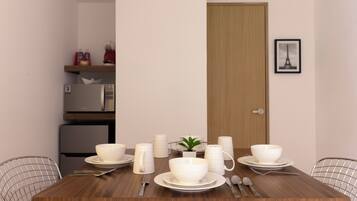 Une table à manger dressée avec de l’assiette, des bols et des couverts blancs, et une petite plante en pot posée sur la table.