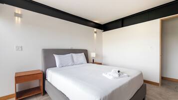 Una habitación de hotel moderna con una cama grande, una mesita de noche, una lámpara y una puerta.