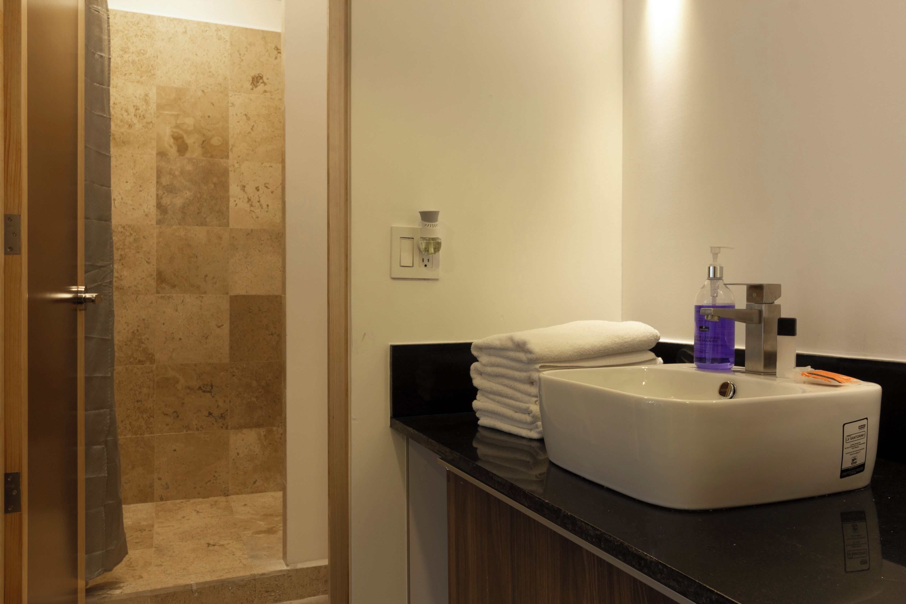 Un baño con lavamanos, espejo, toalla y zona de ducha.