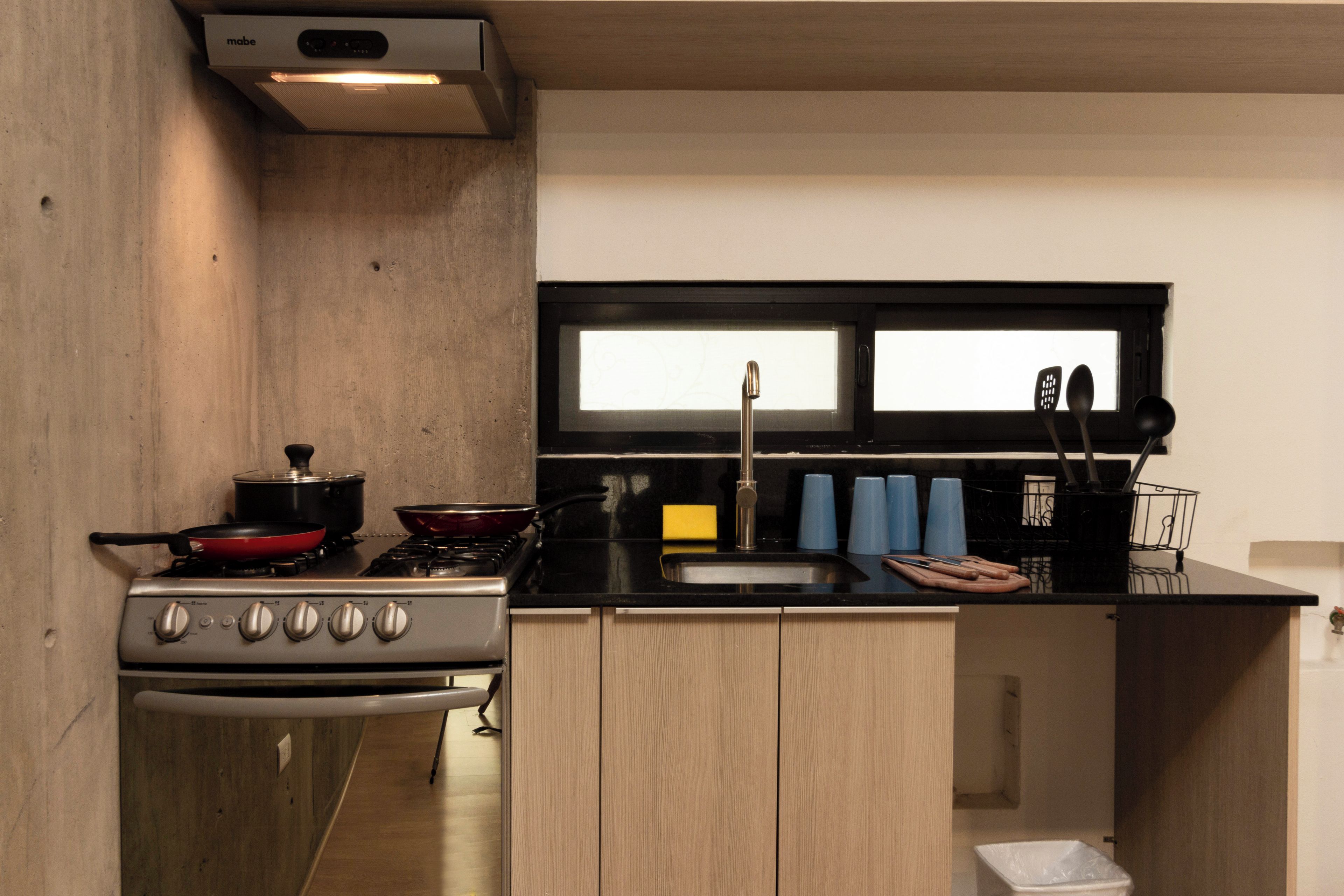 Una cocina compacta con estufa, ollas, pileta y una ventana sobre la encimera.