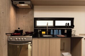 A compact kitchen with a stove, pots, a sink, and a window above the counter. - El Doce By Homirent (Querétaro)