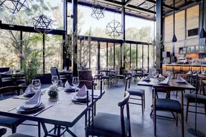 An indoor dining area with tables set for service, large windows, and hanging geometric light fixtures.
