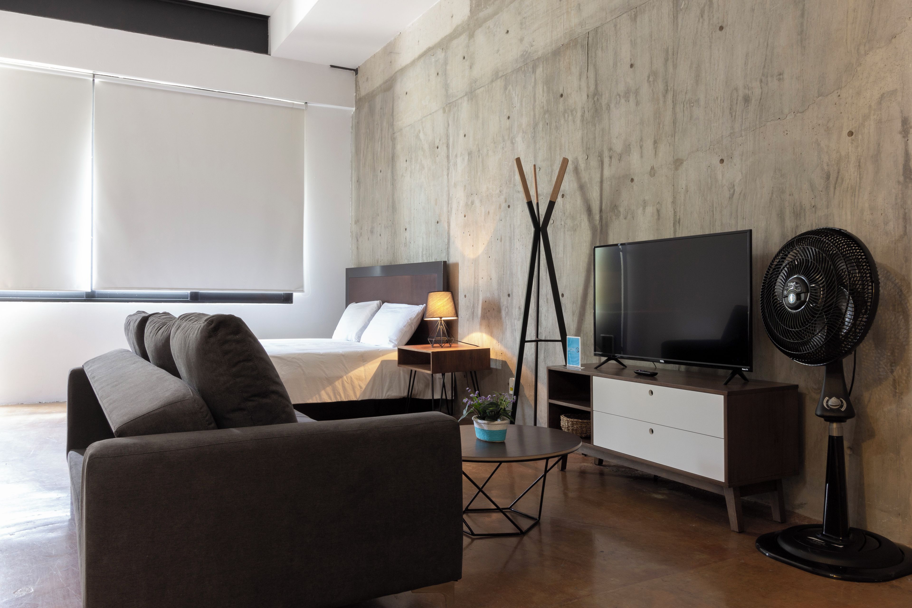 Habitació d'hotel moderna amb llit, sofà, televisió i ventilador de peu.