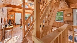 A wooden cabin interior with a staircase, a dining area, and a door leading outside.