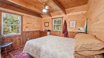 Ein Schlafzimmer einer Holzhütte mit einem Bett, einem Sessel, einem Fenster und einem Deckenventilator.